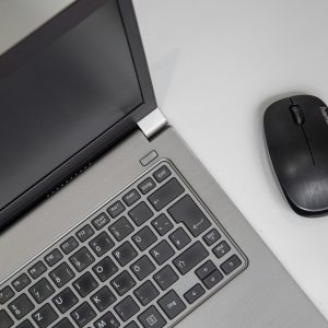 Overhead view of a laptop with a wireless mouse on a white table.